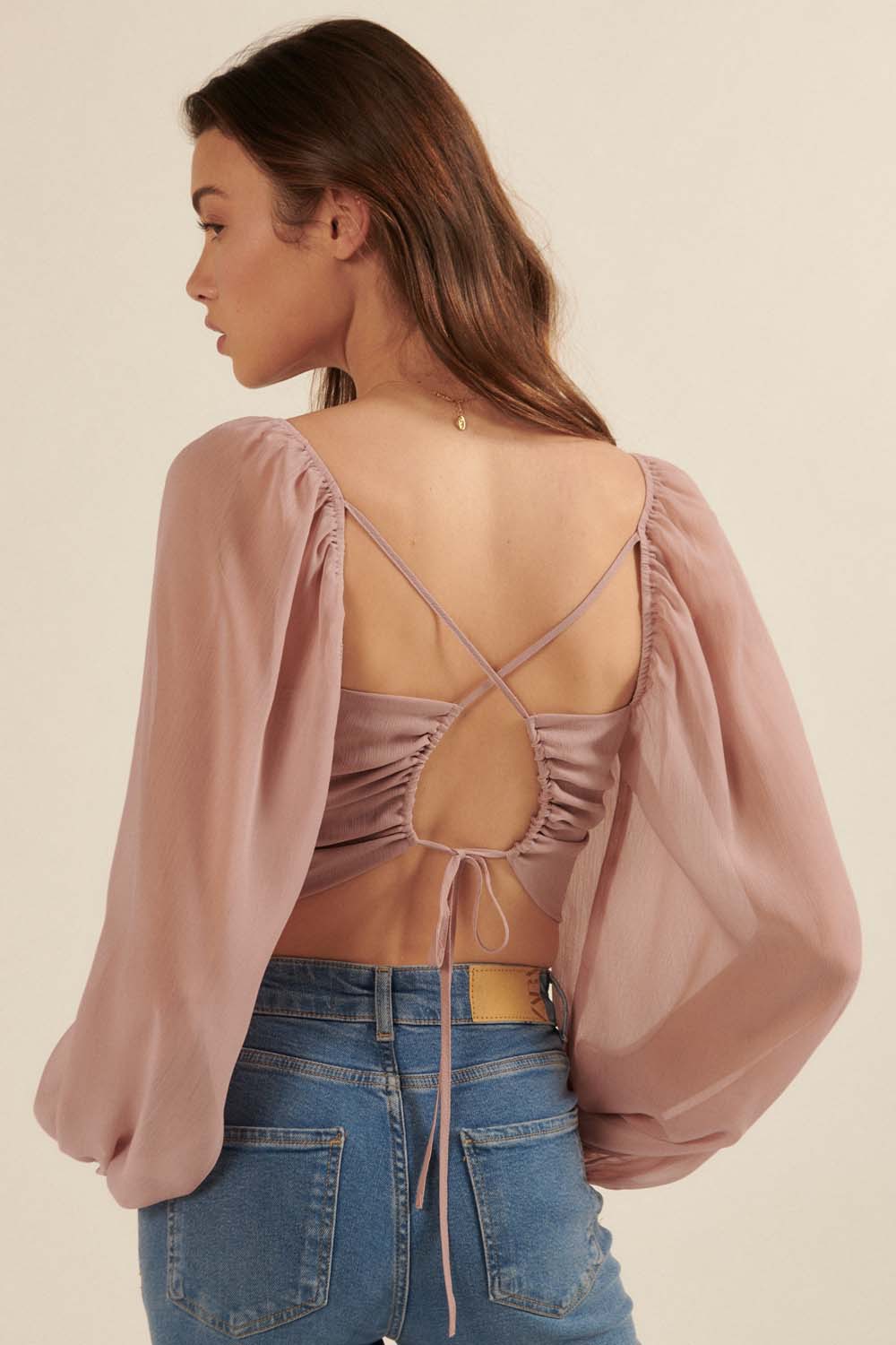 woman wearing a mauve backless blouse with puff sleeves and adjustable drawstring detail, paired with high-waisted jeans