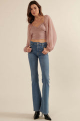 woman wearing a dusty rose cropped top with puff sleeves and high-waisted flared jeans, standing in heeled boots