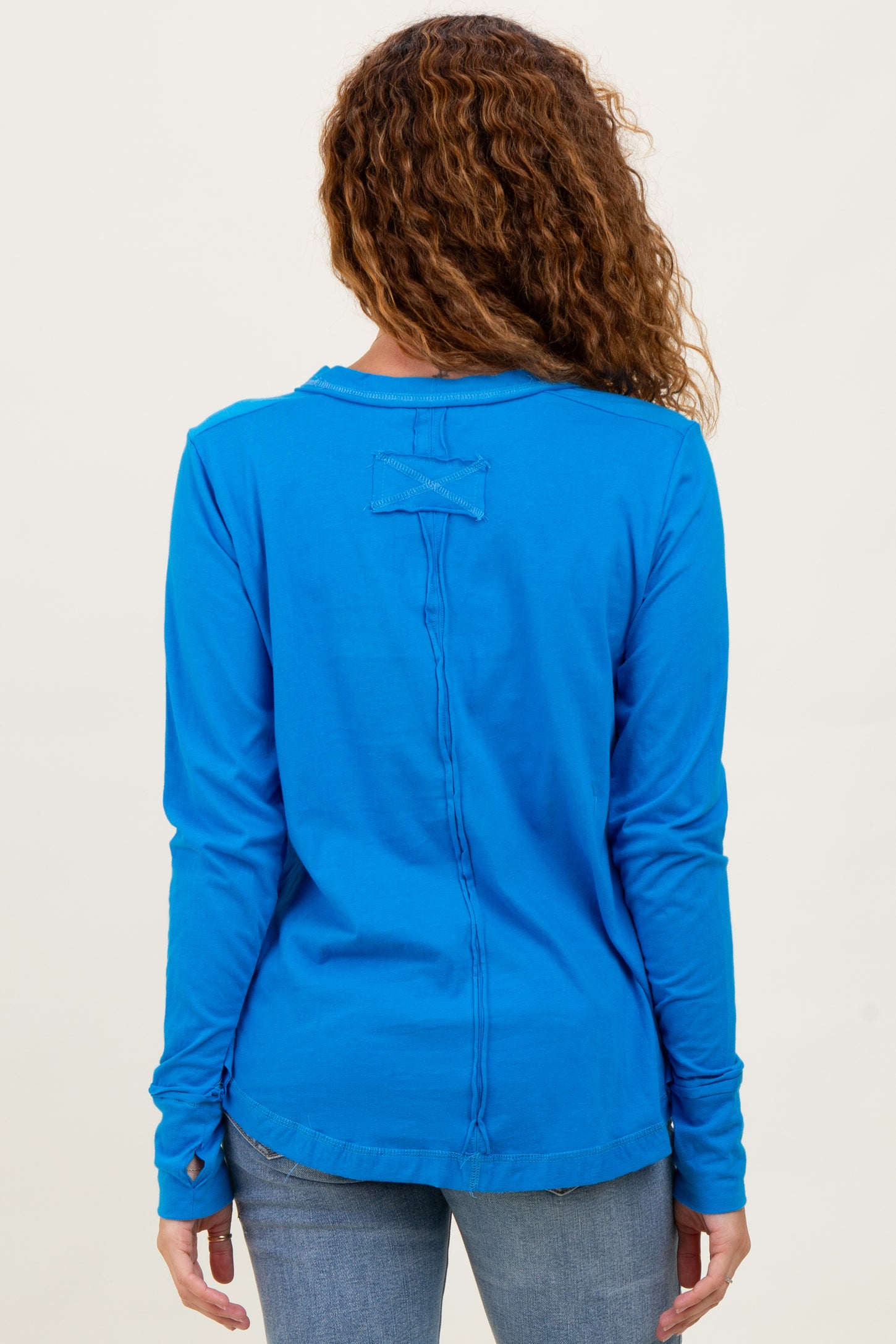 woman wearing a vibrant blue long sleeve top with a unique back seam detail and relaxed fit, viewed from the back