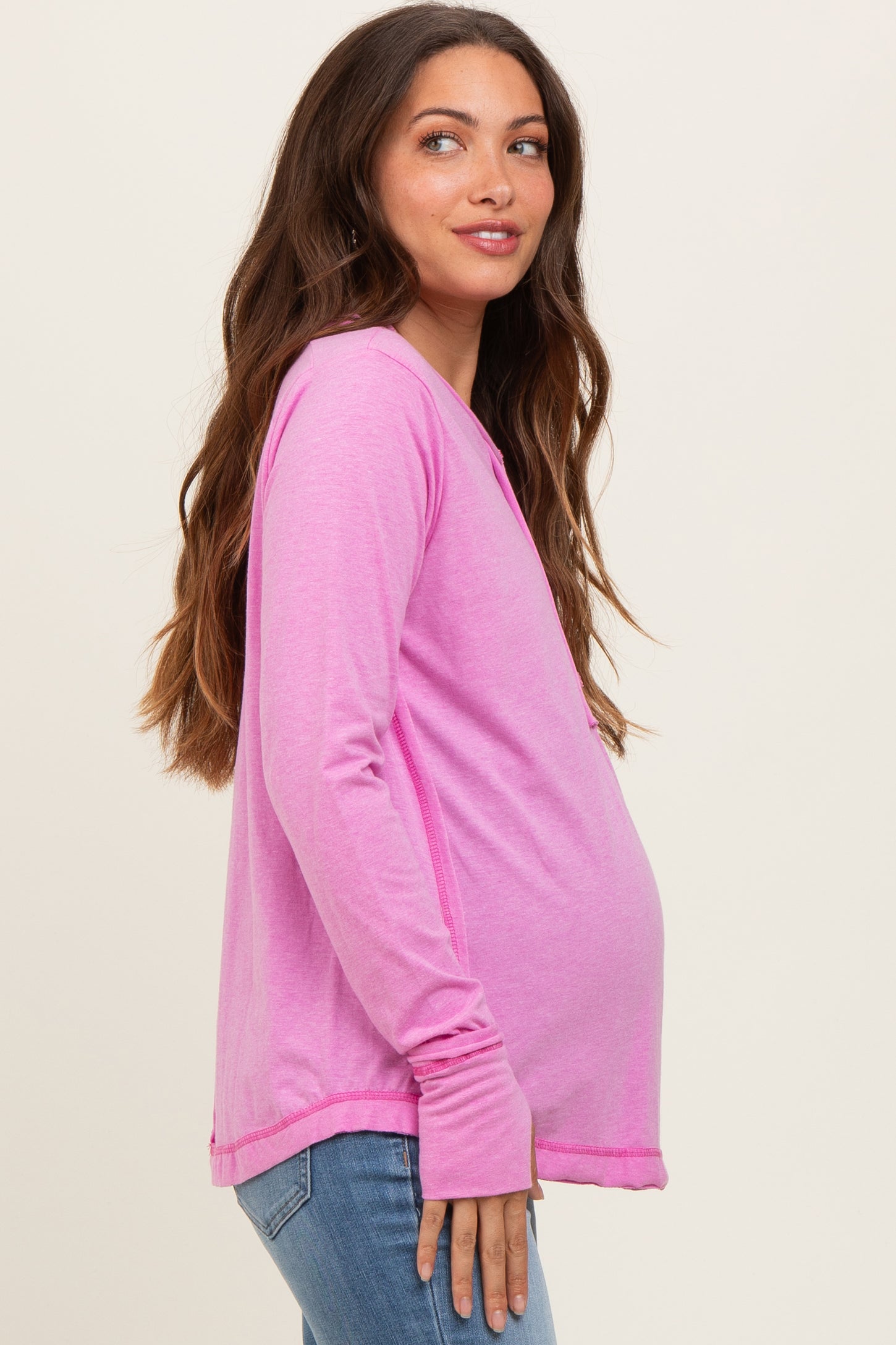 woman wearing a bright pink long sleeve maternity top with a visible baby bump and casual jeans