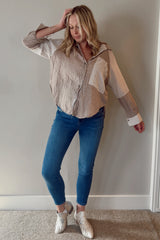 woman wearing a striped maternity button-up shirt with a loose fit and blue skinny jeans, standing against a neutral background