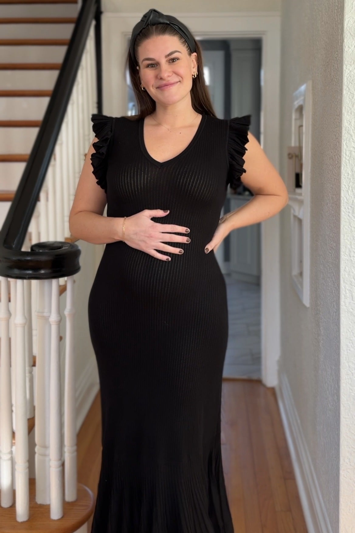 woman wearing a black ribbed maternity dress with ruffle sleeves and holding her baby bump