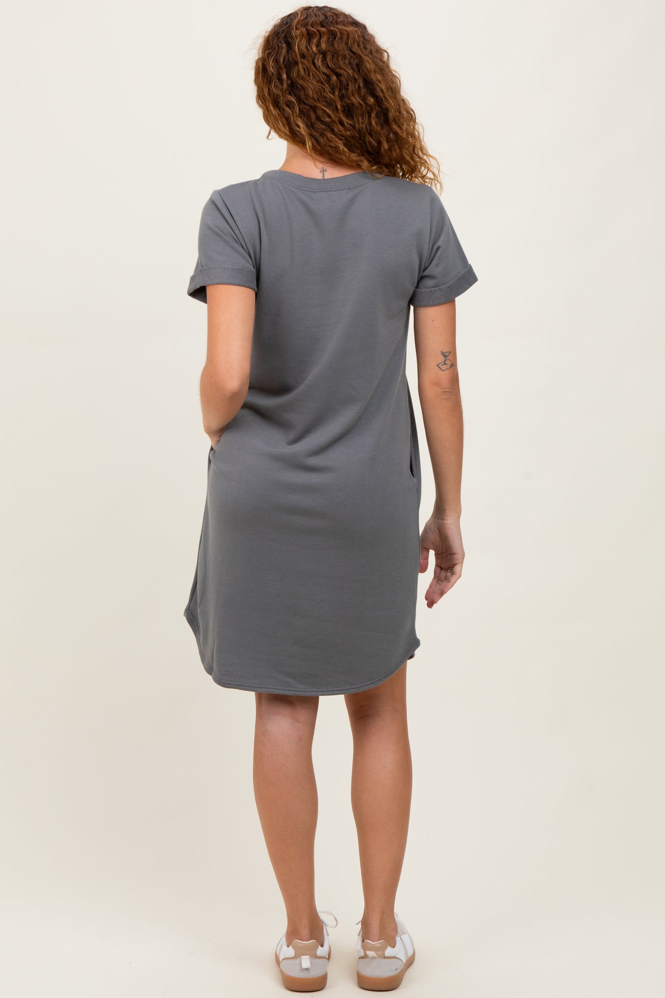 woman wearing a gray short sleeve dress with a relaxed fit and side pockets, viewed from the back