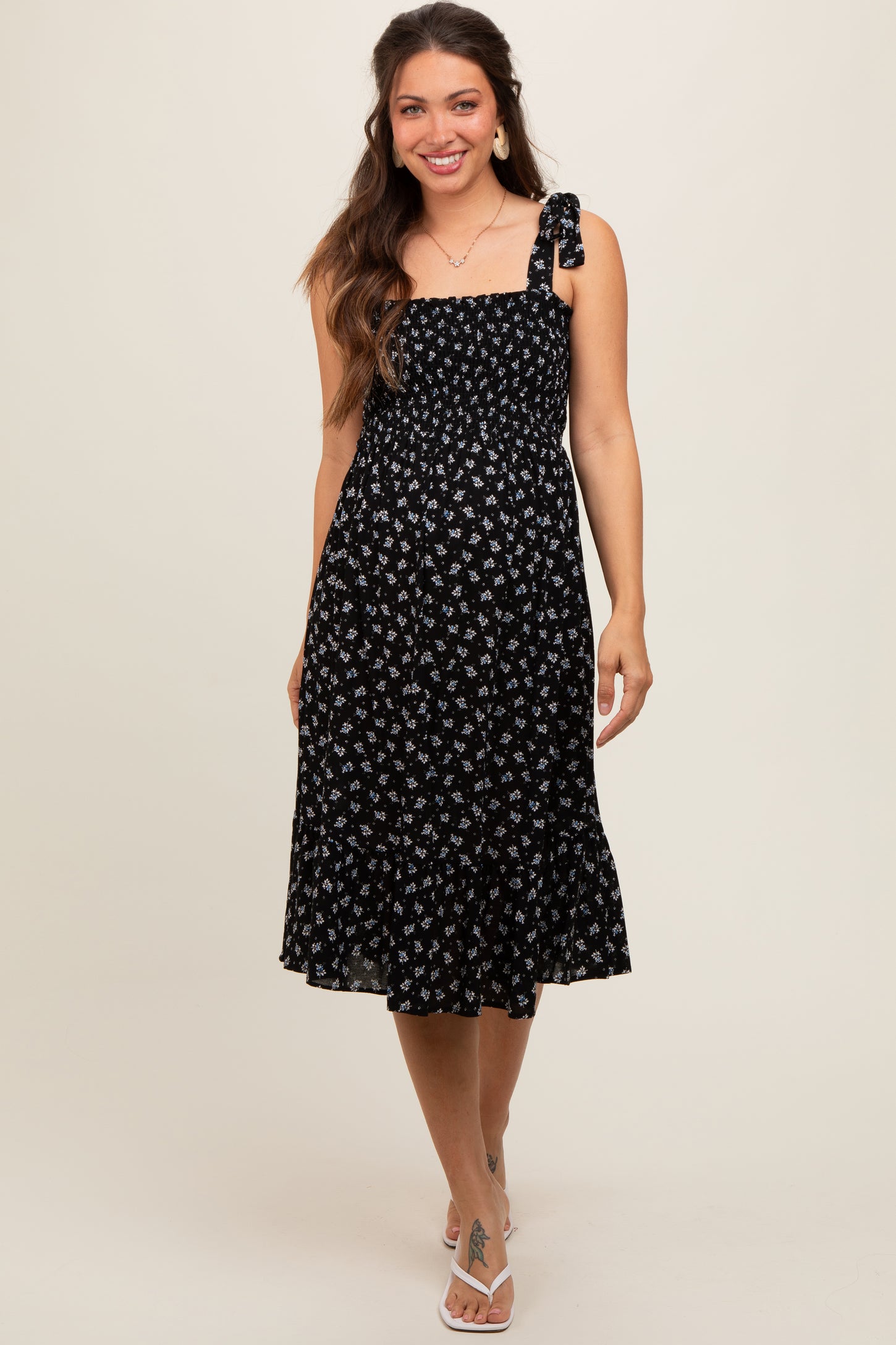 woman wearing a black floral maternity dress with a tie shoulder and a flowy skirt, smiling at the camera