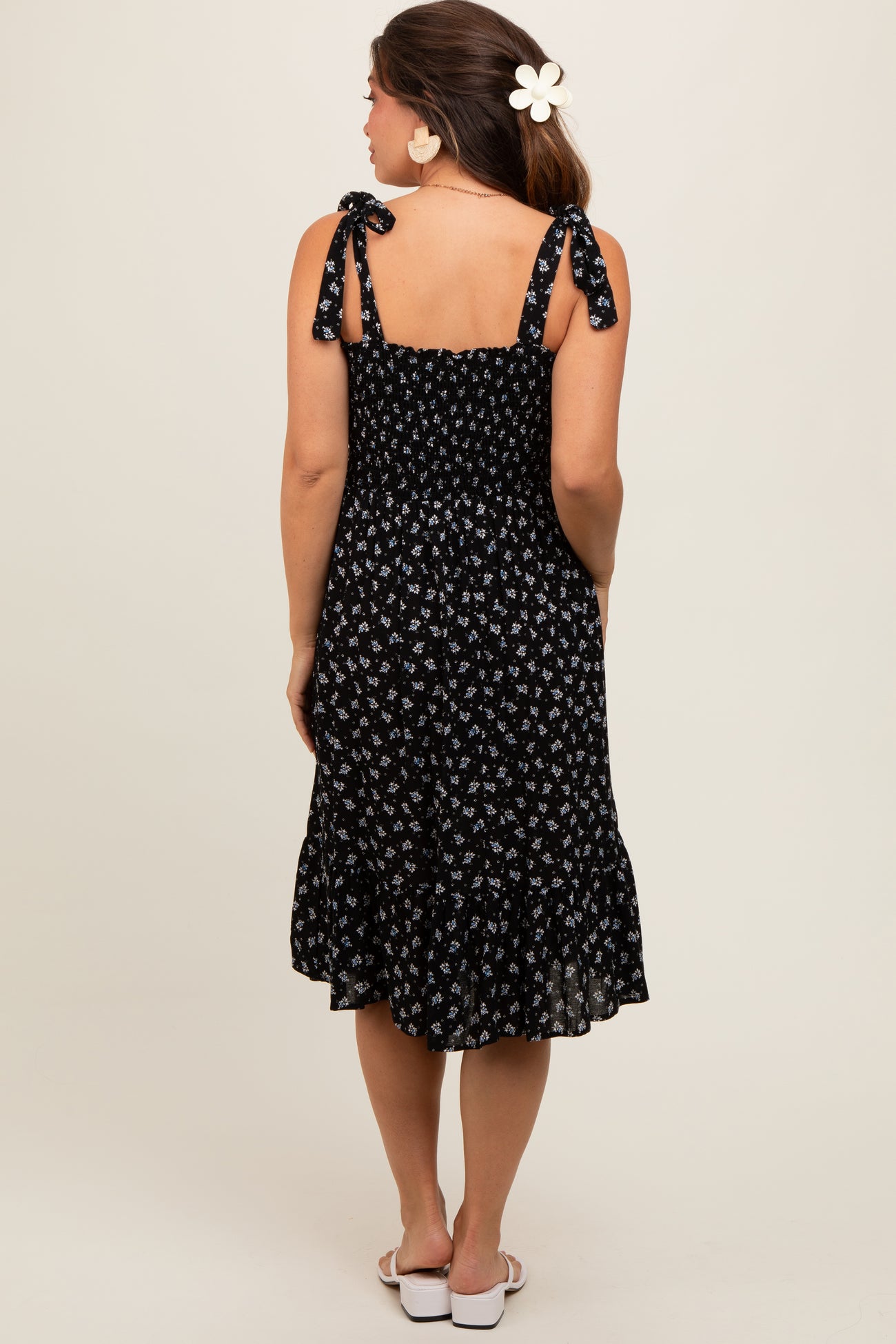 woman wearing a black floral maternity dress with tie straps and a ruffled hem, showing her baby bump from behind