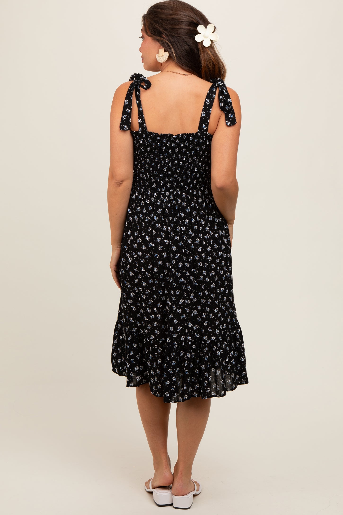 woman wearing a black floral maternity dress with tie straps and a ruffled hem, showing her baby bump from behind