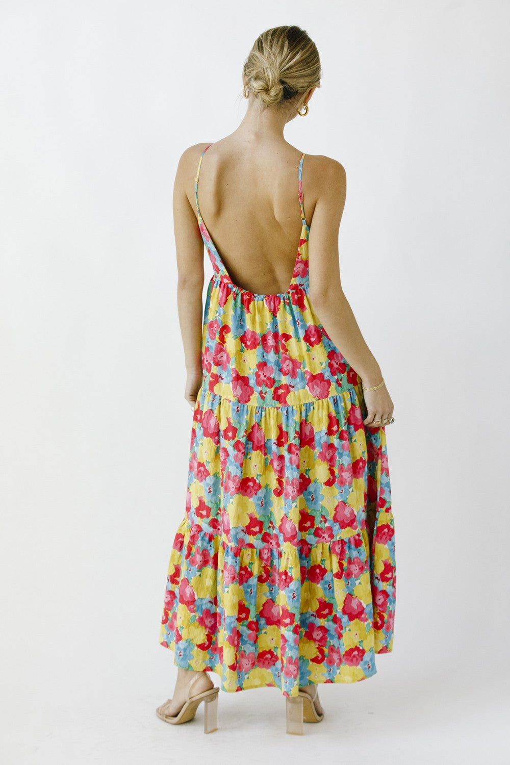 woman wearing a colorful floral maxi dress with a low back and tiered design, standing with her back to the camera