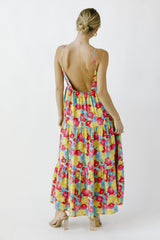 woman wearing a colorful floral maxi dress with a low back and tiered design, standing with her back to the camera