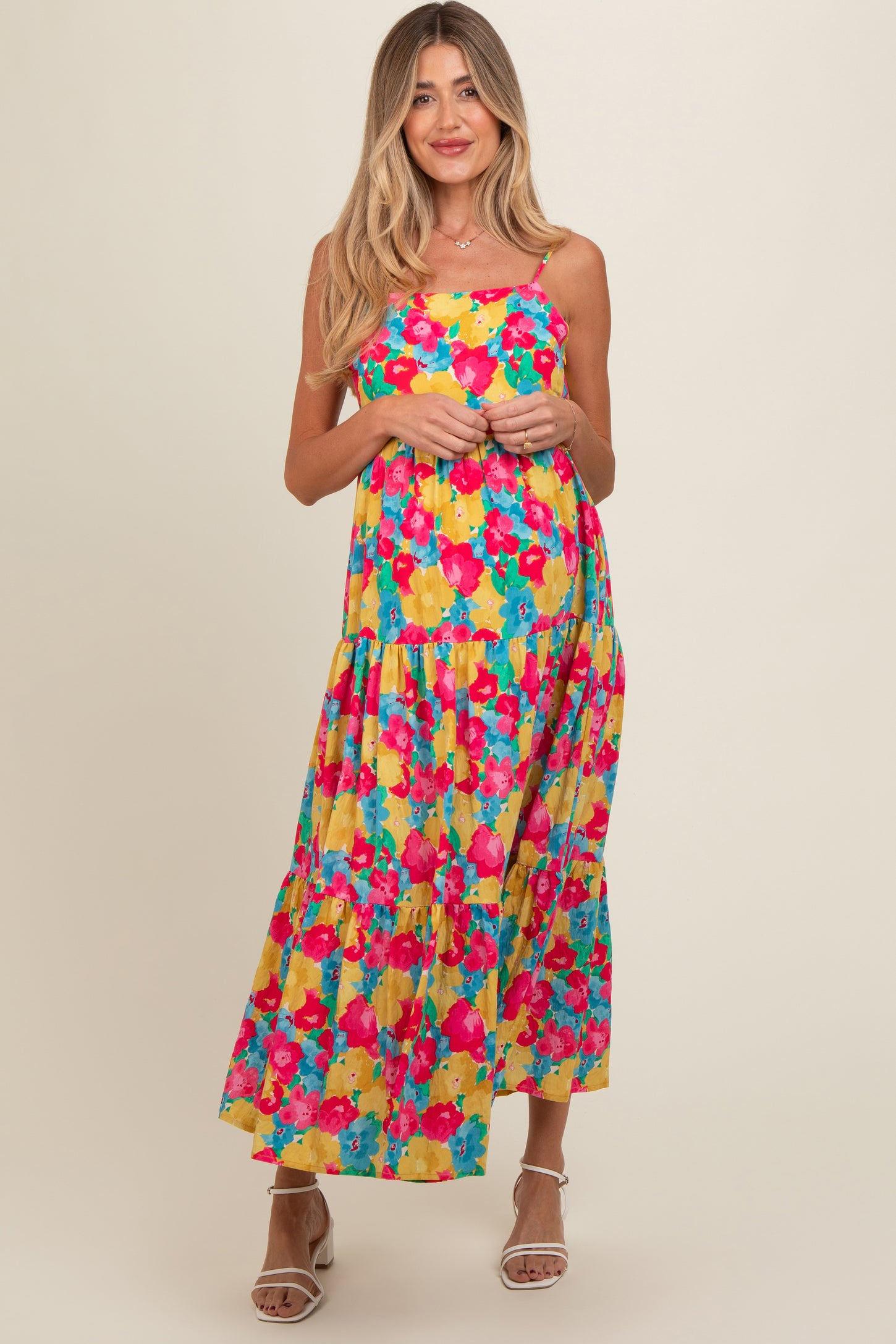 woman wearing a colorful floral maternity maxi dress with a tiered skirt and spaghetti straps, smiling at the camera