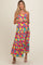 woman wearing a colorful floral maternity maxi dress with a tiered skirt and spaghetti straps, smiling at the camera