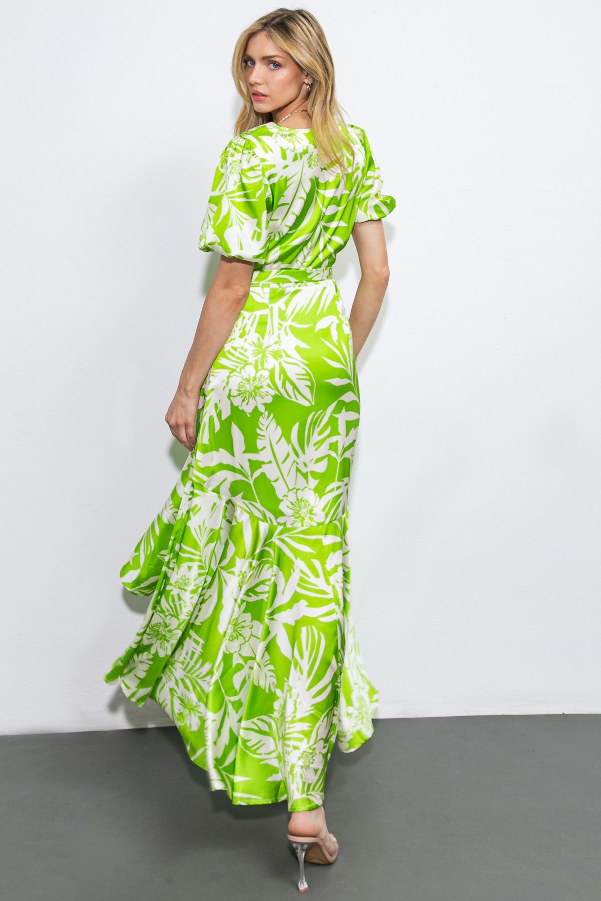 woman wearing a green floral maxi dress with puff sleeves and a ruffled hem, seen from the back
