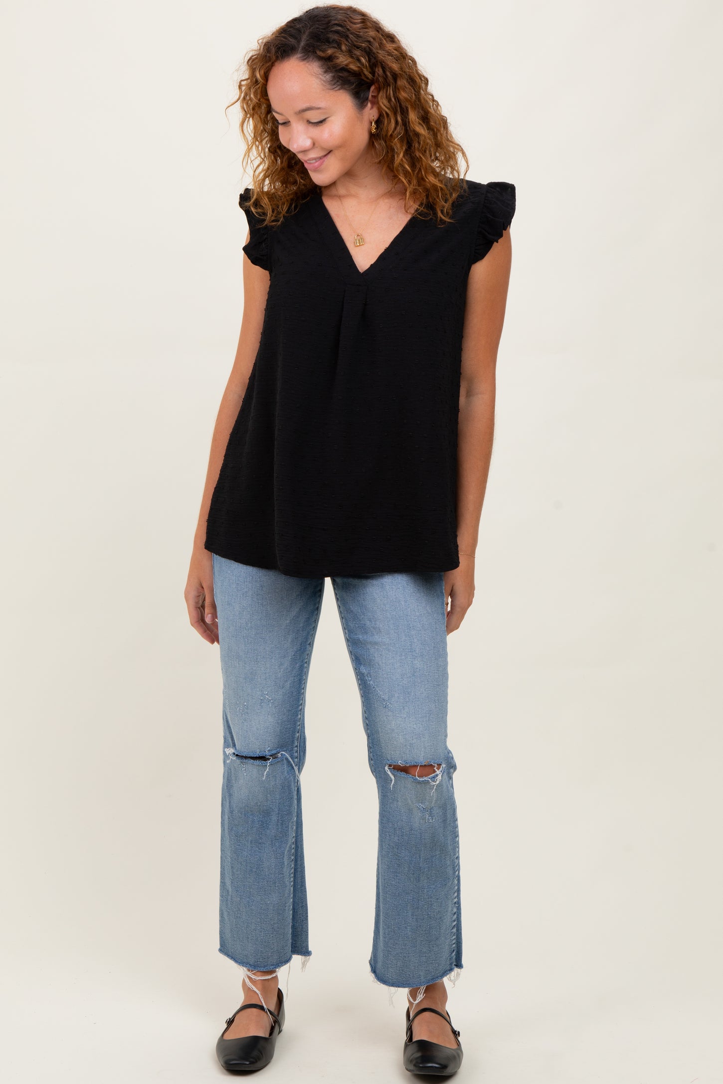 woman wearing a black ruffled sleeve top and distressed light blue flared jeans, standing and smiling