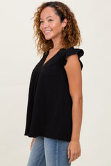 woman wearing a black sleeveless top with ruffle details and a relaxed fit, paired with blue jeans