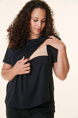 woman wearing a black short sleeve top, lifting the fabric to reveal a beige nursing bra underneath