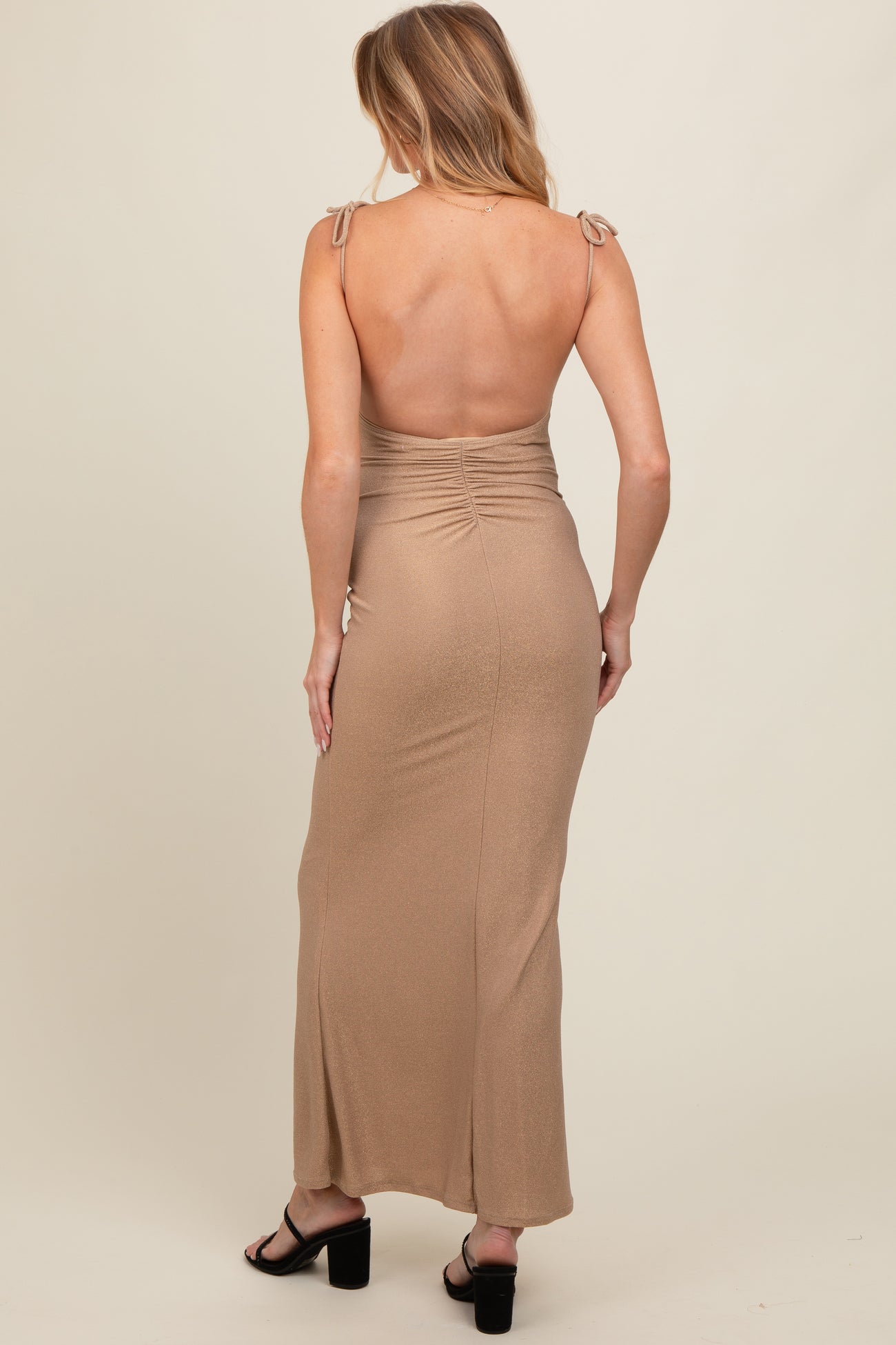 woman wearing a backless tan maternity maxi dress with tie straps and ruching detail