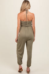 woman wearing an olive green maternity jumpsuit with a halter neck and relaxed fit, showing no baby bump.