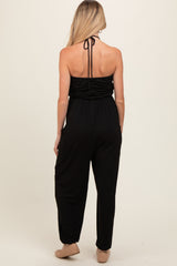 woman wearing a black maternity jumpsuit with a halter neck and gathered back details, showing a sleek silhouette