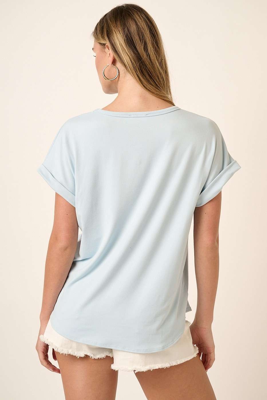 woman wearing a light blue short sleeve top with rolled cuffs and relaxed fit, standing with her back to the camera
