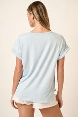 woman wearing a light blue short sleeve top with rolled cuffs and relaxed fit, standing with her back to the camera