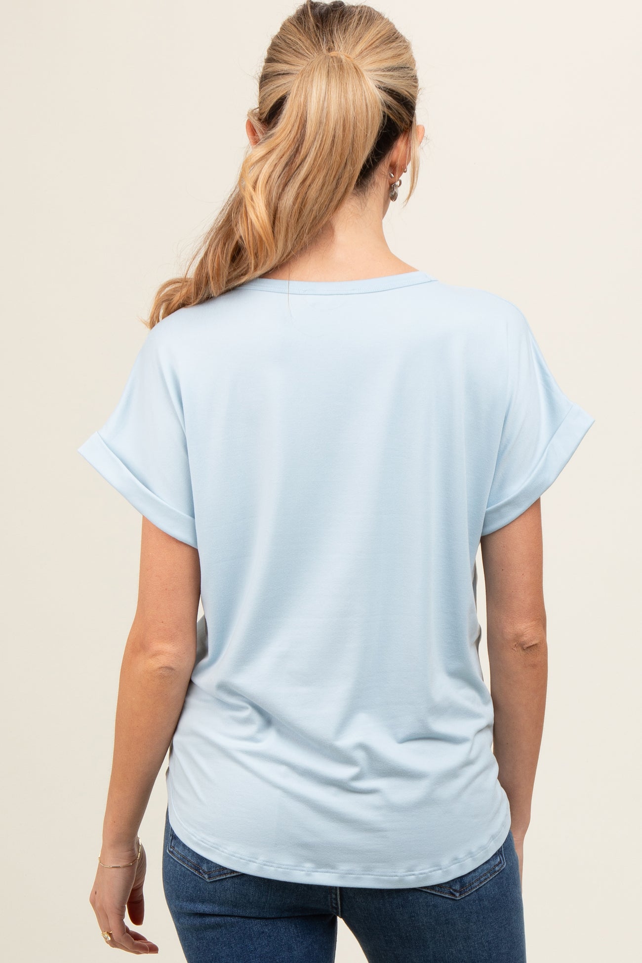 woman wearing a light blue short sleeve maternity top, viewed from the back, paired with dark jeans