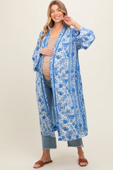 woman wearing a blue floral maternity kimono over a tan top and showing her baby bump, paired with jeans and sandals