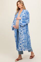 woman wearing a blue floral maternity kimono over a beige top and showing her baby bump while standing