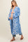woman wearing a blue floral maternity kimono over a beige top and showing her baby bump while standing