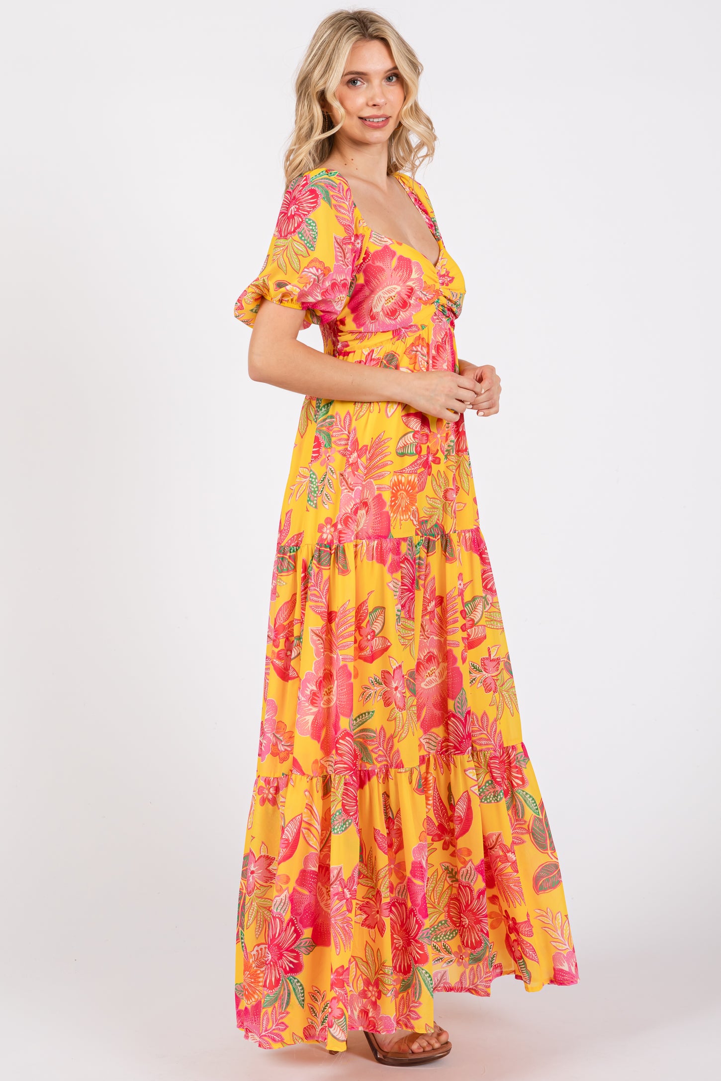 woman wearing a bright yellow floral maxi dress with puff sleeves and a tiered skirt, standing sideways