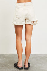 woman wearing light beige distressed denim shorts with frayed hem and cut-out details, viewed from the back
