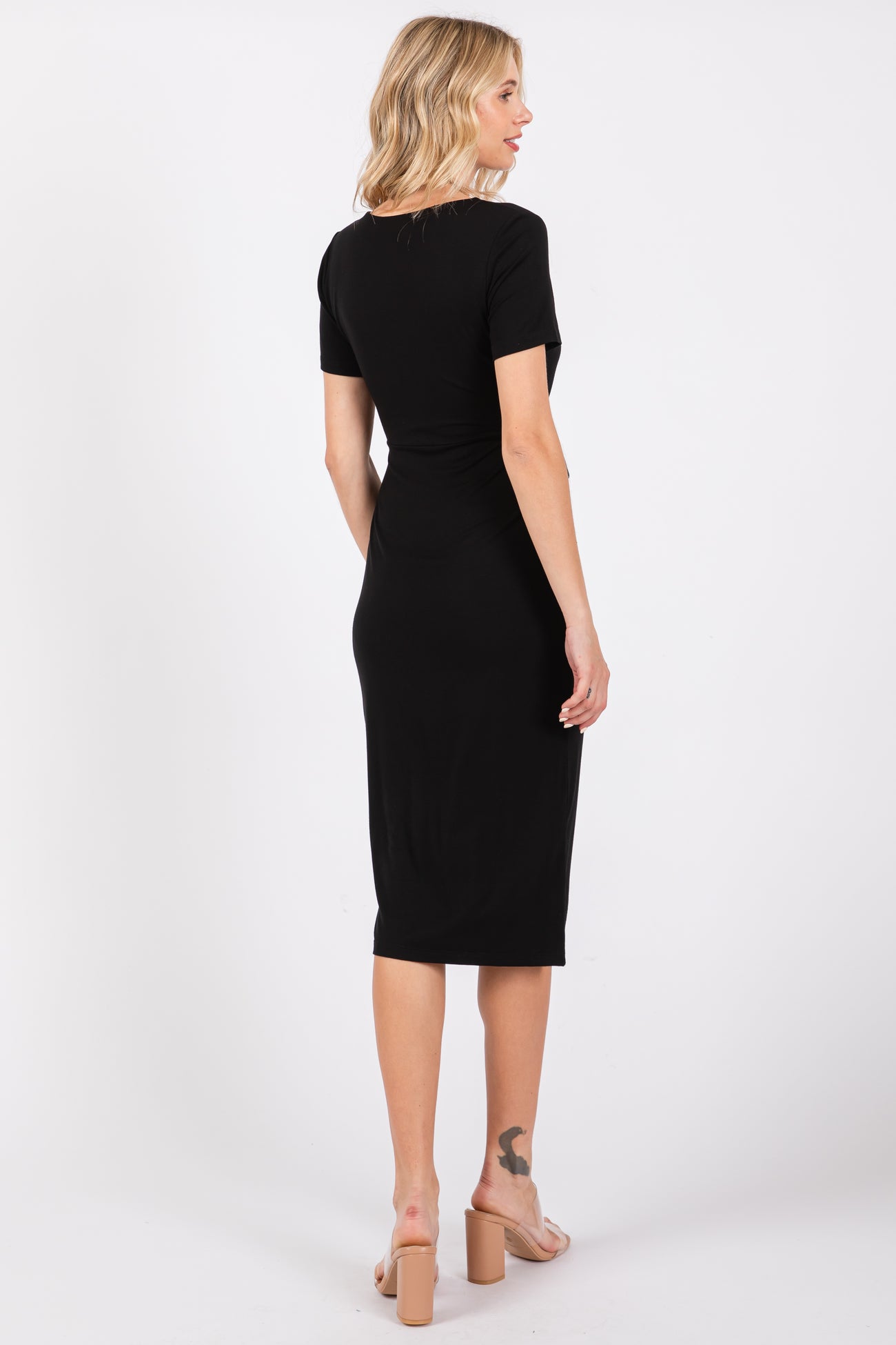 woman wearing a black short sleeve fitted midi dress, showing the back view and paired with beige heeled sandals