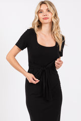 woman wearing a black knee-length dress with a square neckline and tied waist detail
