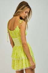 woman wearing a bright yellow floral mini dress with tie straps and layered ruffle detailing