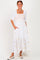 woman wearing a white maxi dress with yellow floral embroidery and puff sleeves, standing with hands in pockets