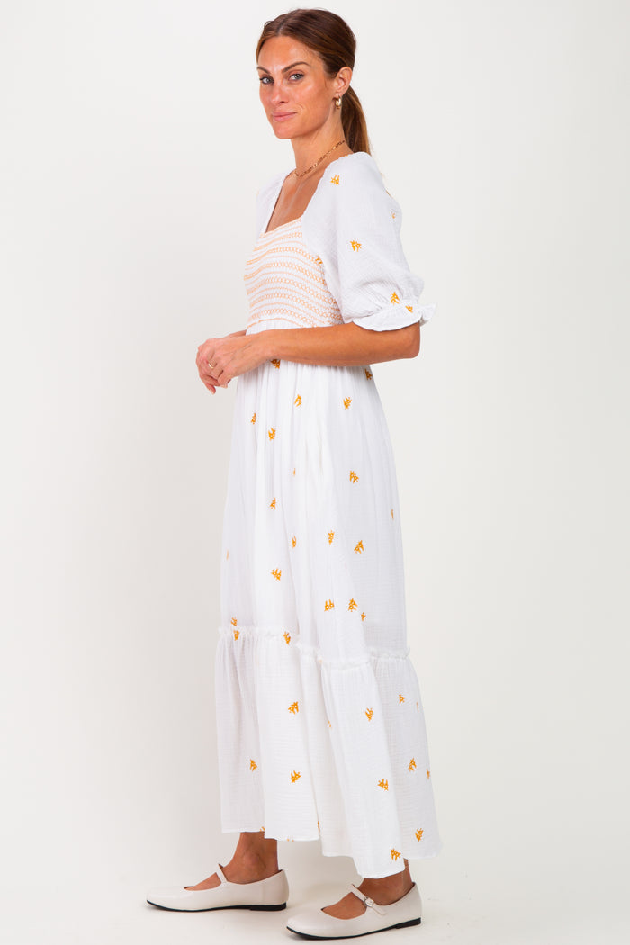 woman wearing a white floral maxi dress with puff sleeves and a smocked bodice, standing sideways against a plain background