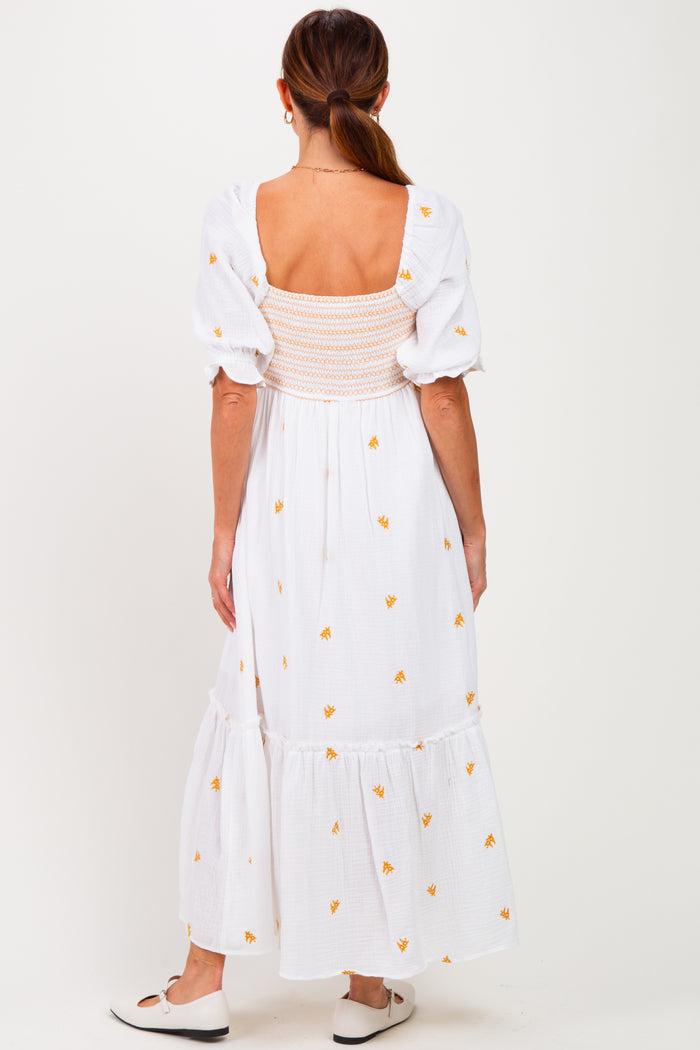 woman wearing a white maxi dress with floral embroidery and a smocked back, seen from the back