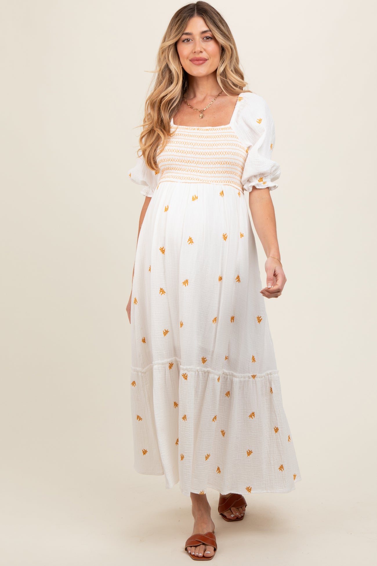 woman wearing a white maternity dress with floral embroidery and puff sleeves, showcasing her baby bump