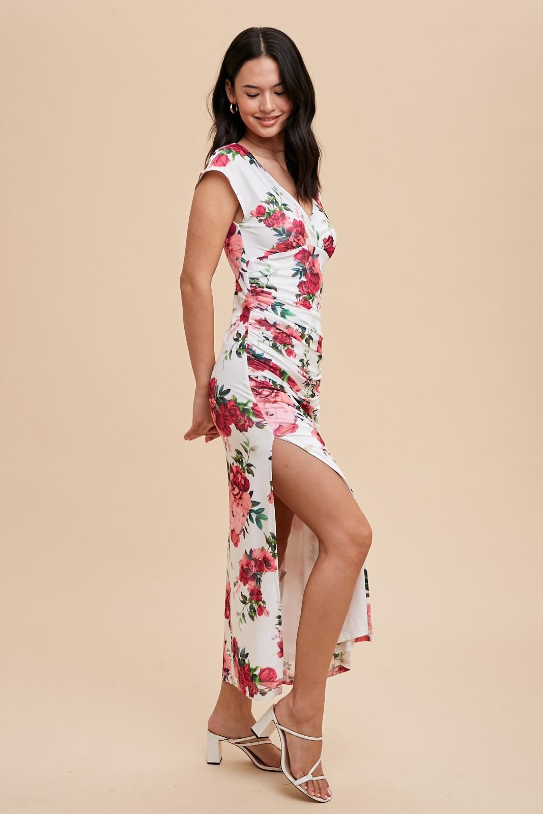woman wearing a floral wrap maxi dress with a high slit and short sleeves, standing against a beige background