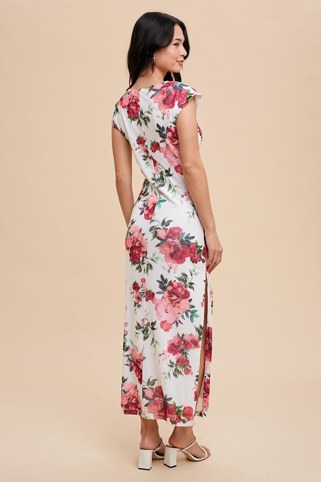 woman wearing a white floral maxi dress with cap sleeves and side slits, standing against a light beige background