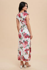 woman wearing a white floral maxi dress with cap sleeves and side slits, standing against a light beige background