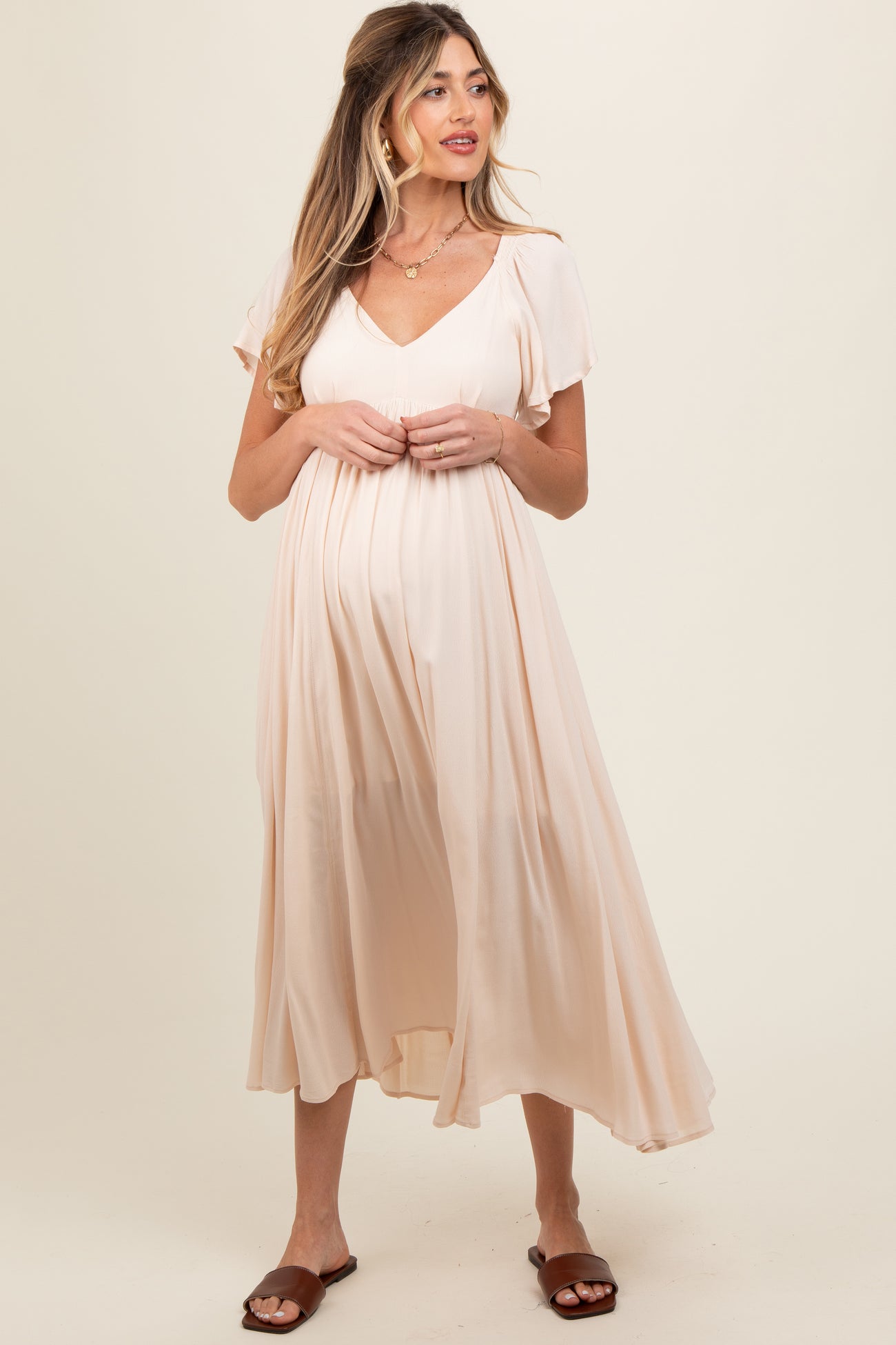 woman wearing a light peach maternity dress with short sleeves and a flowing silhouette, showing her baby bump