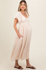 woman wearing a blush pink maternity maxi dress with short ruffle sleeves and side pockets, showcasing her baby bump