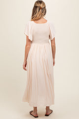 woman wearing a light pink maternity maxi dress with short flutter sleeves and a smocked bodice, showing her baby bump