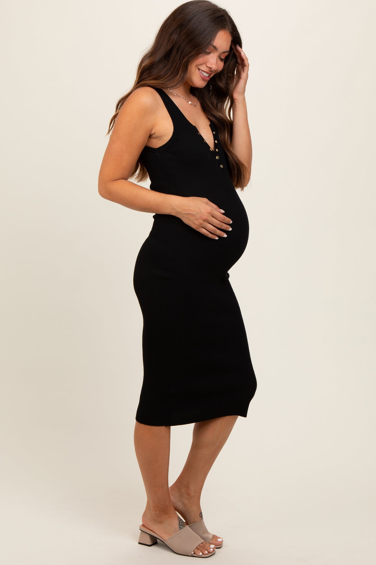 woman wearing a black ribbed maternity dress with buttons, showing her baby bump and styled with light-colored heels