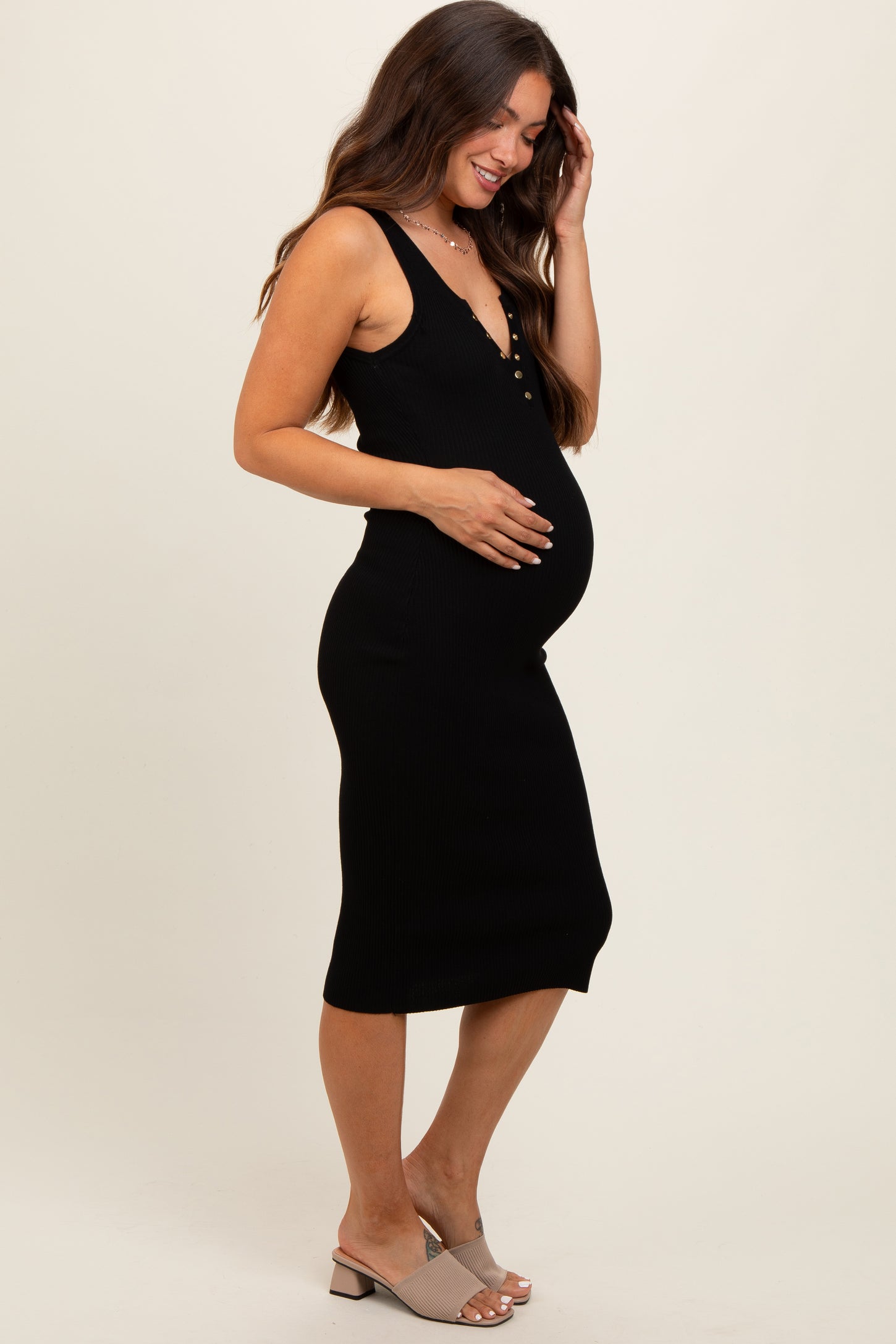 woman wearing a black ribbed maternity dress with buttons, showing her baby bump and styled with light-colored heels