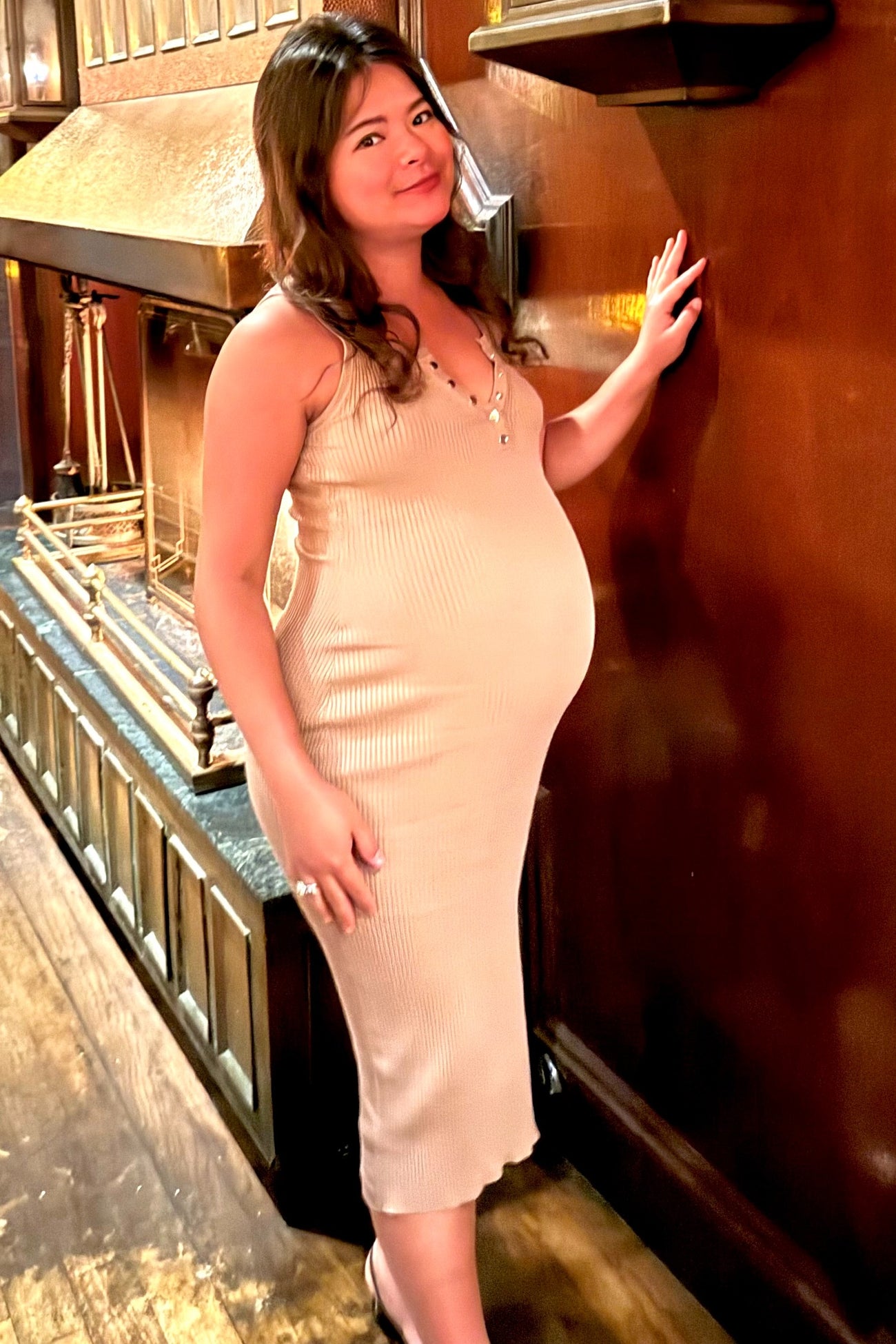 woman wearing a beige ribbed maternity dress with a fitted silhouette, showing her baby bump while posing indoors