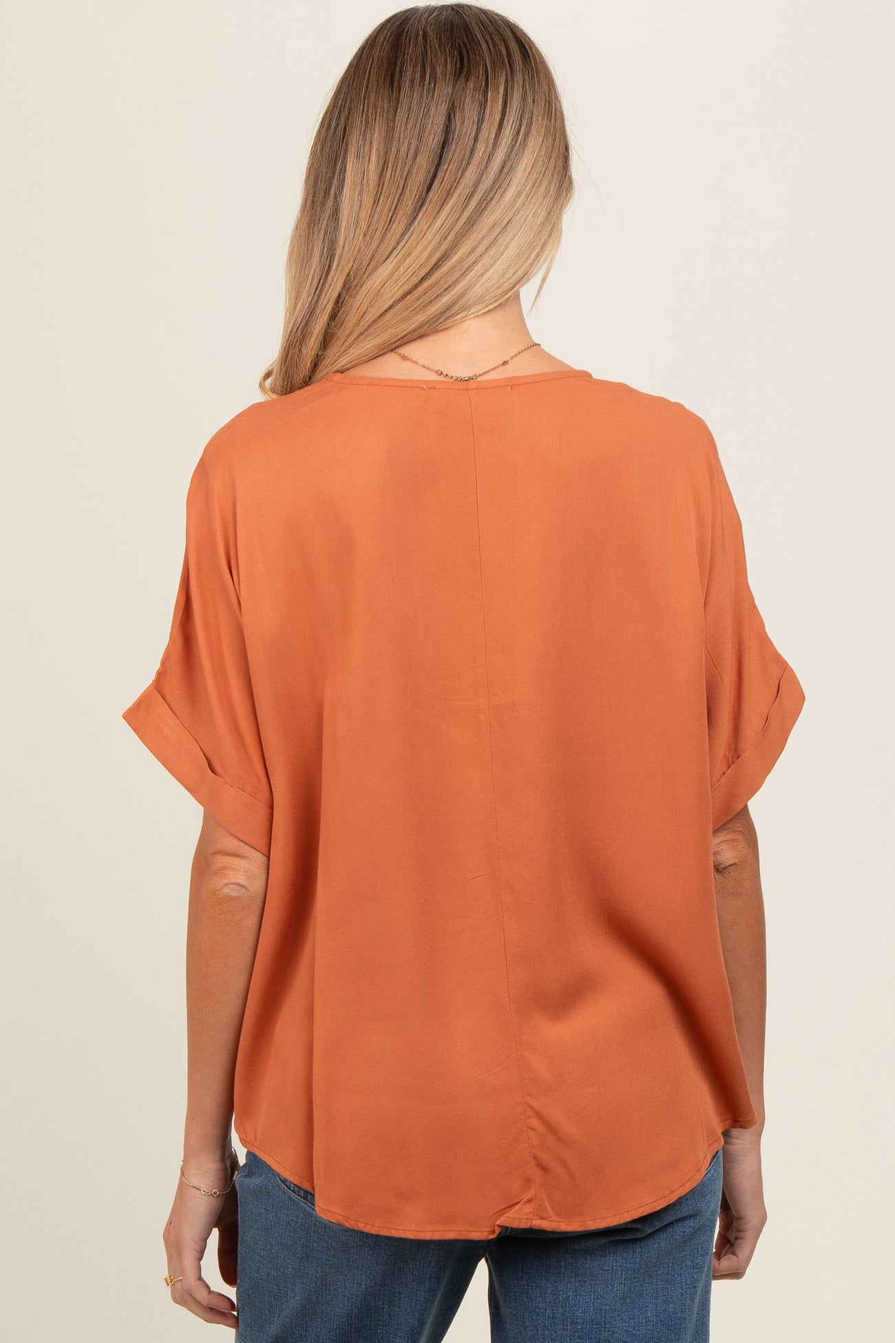 woman wearing a rust-colored maternity top with rolled sleeves, viewed from the back