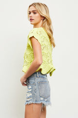 woman wearing a bright yellow knitted crop top with a scalloped hem and paired with distressed denim shorts