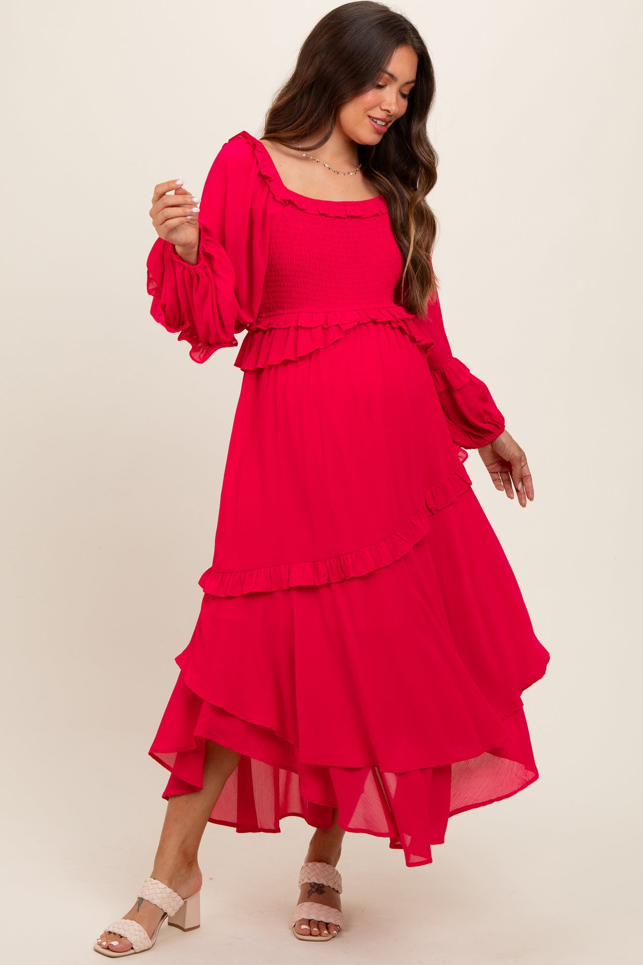 woman wearing a bright pink maternity dress with ruffle details and long sleeves, showcasing her baby bump