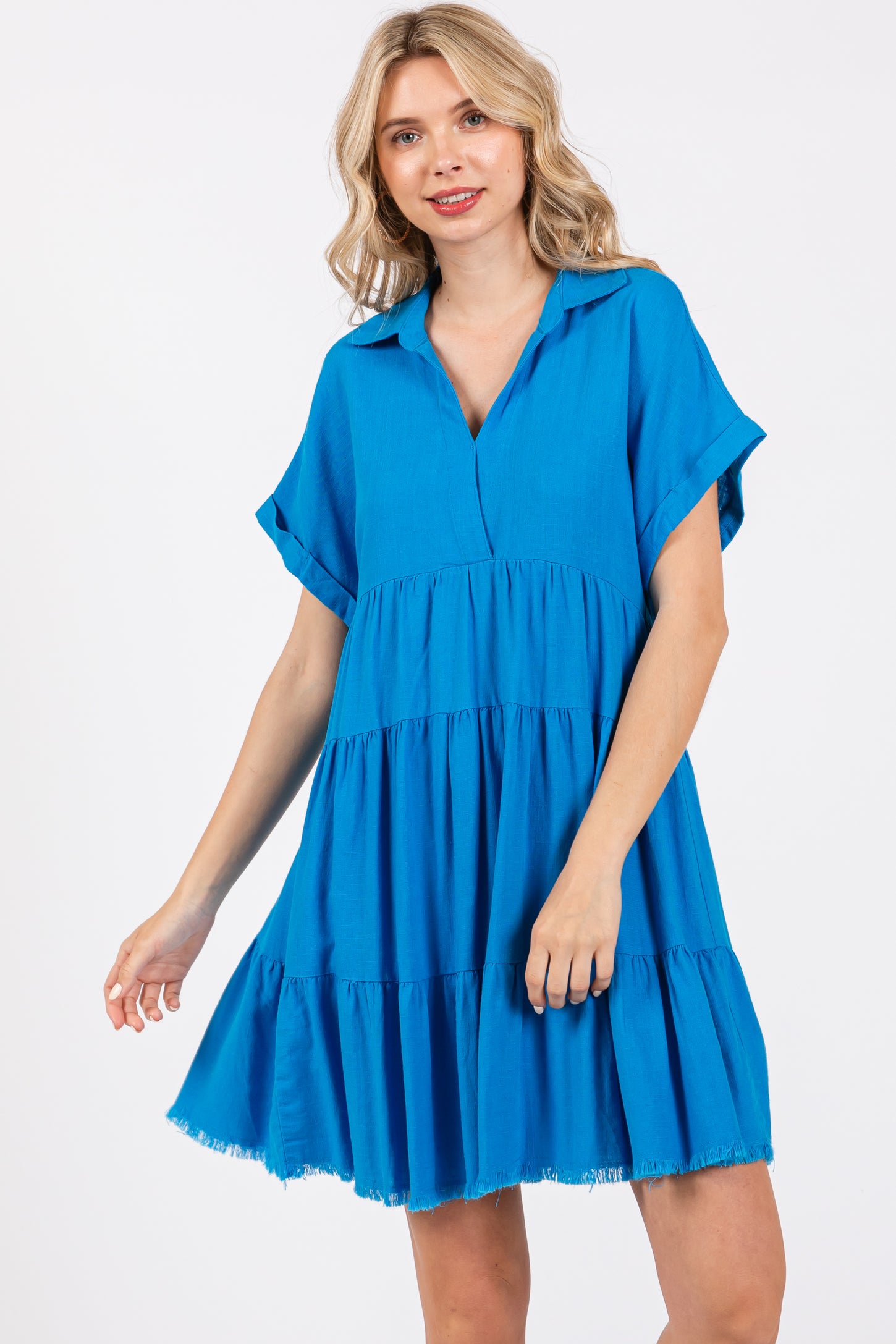 woman wearing a bright blue short sleeve tiered dress with a collar and frayed hemline