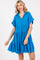 woman wearing a bright blue short sleeve tiered dress with a collar and frayed hemline